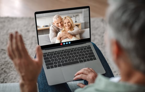 A person waves while communicating via call, engaging with a happy couple who are smiling at the screen. The setting is a cozy indoor environment, embodying warmth and connection. photo