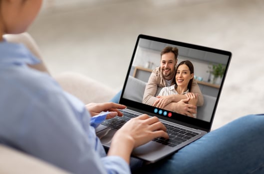 A woman sits comfortably on a couch, connecting with a friendly couple through a call on her laptop, showcasing a warm and engaging conversation in a cozy setting. photo