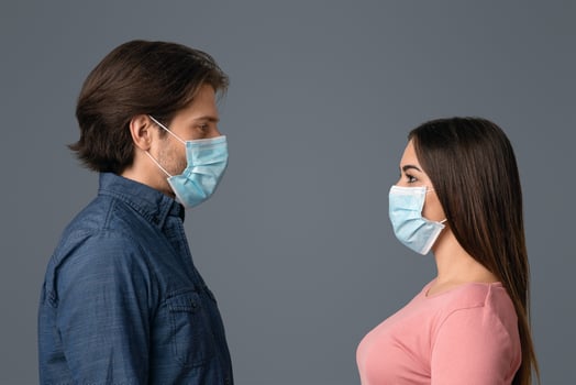 Social Distancing Concept. Side View Of Young Man And Woman In Medical Masks Standing Face To Face Over Light Studio Background, Empty Space photo