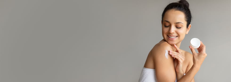 A young woman smiles as she gently applies moisturizer to her shoulder, showcasing a relaxing moment in a simple indoor environment, focusing on skincare and self-care. photo