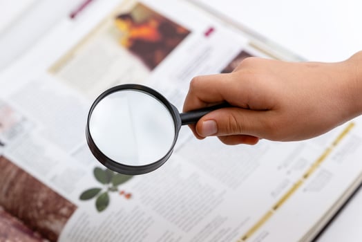 Hand holding magnifying glass examining book and plant inside, symbolizing research, knowledge, nature exploration, and learning through books photo