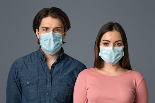 Coronavirus Concept. Portrait of young caucasian couple in protective medical masks standing over light background in studio, free space photo