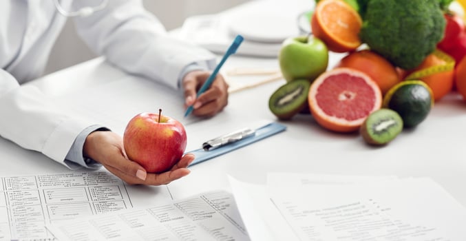Doctor dietologist giving apple to afro woman patient during session, close up photo