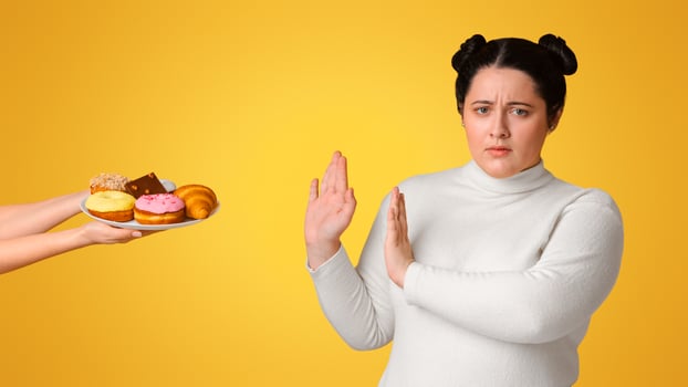 Diet Concept. Fatty girl refusing consume tasty delicious sweets on plate, rejecting unhealthy junk food, isolated on yellow background, copy space photo