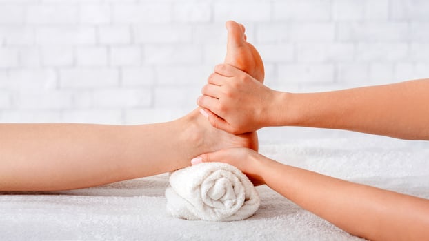 Foot massage in spa salon. Masseur does procedure on table with white towels on white brick background, free space photo