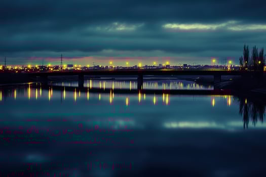 A bridge over a calm river with city lights reflected in the water under a dark sky. photo