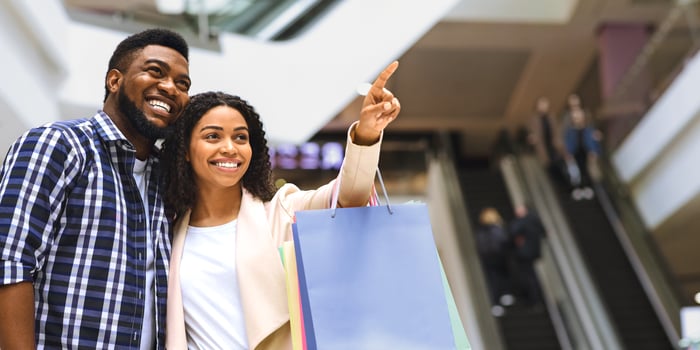 Black Millennial Couple Shopping Together In Mall, Young Woman Carrying Shopper Bags And Pointing At Showcase With New Clothes, Copy Space photo