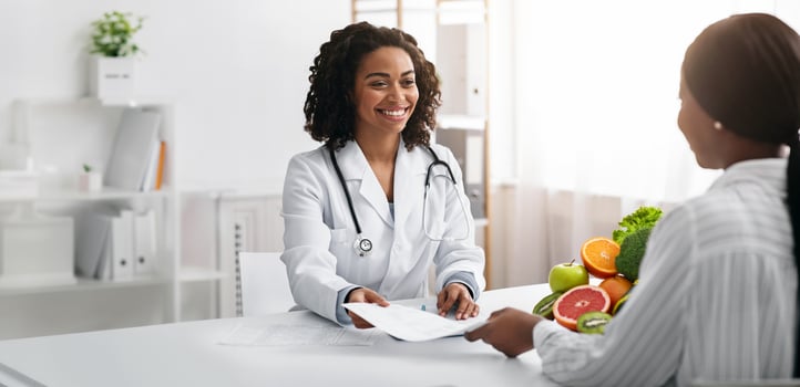 Personal diet. Cheerful african american female dietologist giving diet plan to woman client, clinic interior photo