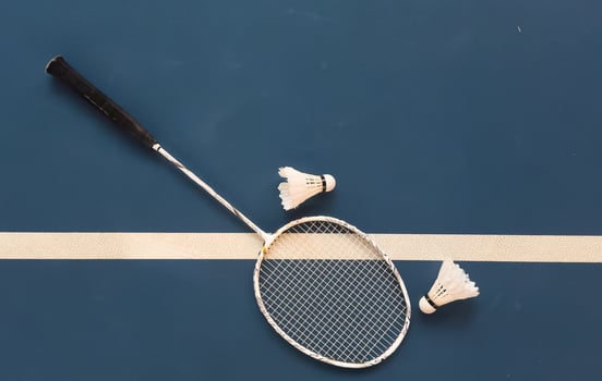 Cream white badminton shuttlecock and racket with neon light shading on dark floor in indoor badminton court, copy space, soft and selective focus. photo
