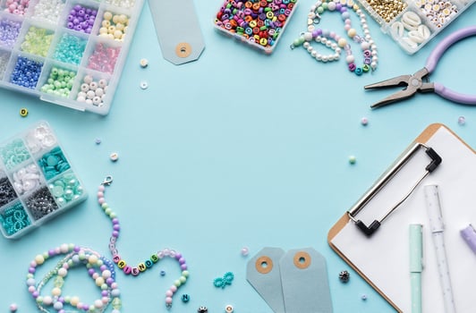 Colorful beads, pliers, clipboard and price tags arranged on blue surface for diy bracelet making photo