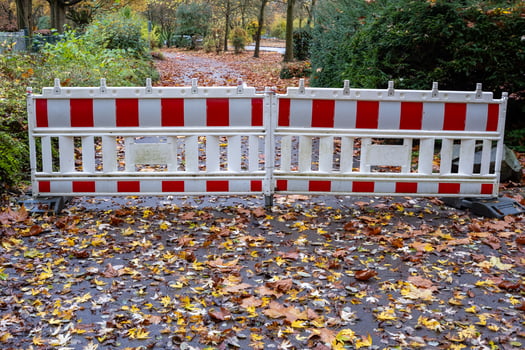 Red and white construction barrier blocking access to park path covered with autumn leaves photo