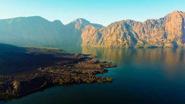 Aerial from the summit of Rinjani shows the stunning Segara Anak Lake below, Surrounded by vibrant blue skies and clouds, the lake's serene beauty stands out against the dramatic landscape. photo