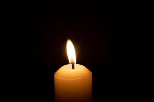 A single burning candle flame or light glowing on a big white candle isolated on black or dark background on table in church for Christmas, funeral or memorial service photo