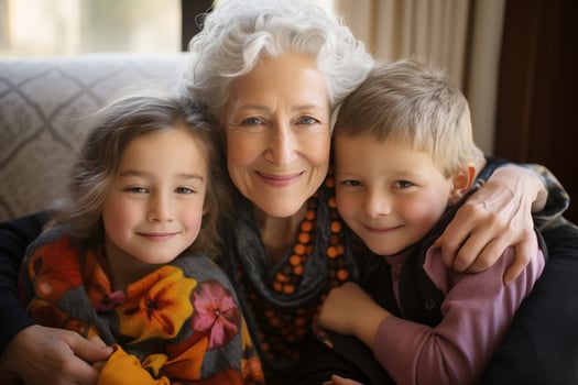 happy caucasian grandmother hugs grandchildren boy and girl, all looking at camera and smiling. photo from inside the house