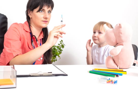The doctor holds a medical syringe in his hands and a little girl cries nearby in fright. The concept of fear of vaccinations and injections in children, copy space photo