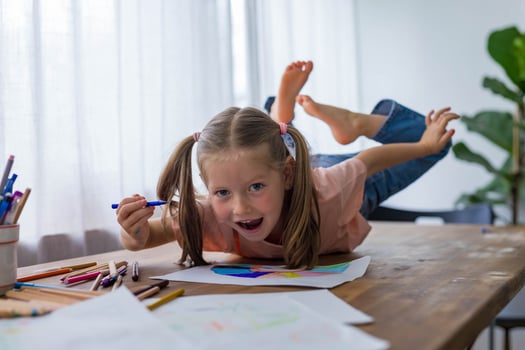 With smile 5-year-old girl giggles while creating art at the table with vibrant colored pencils photo