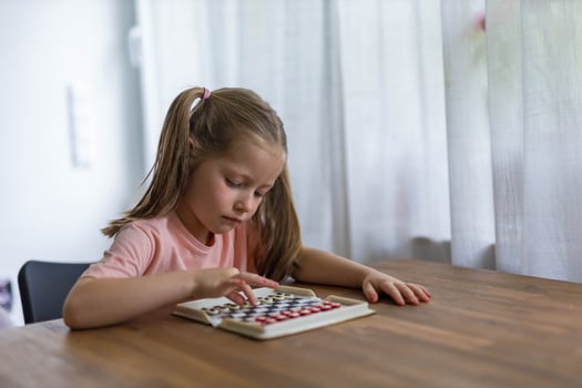 Focused 5-year-old girl plays mini chess, planning her next move in a playful, educational moment photo
