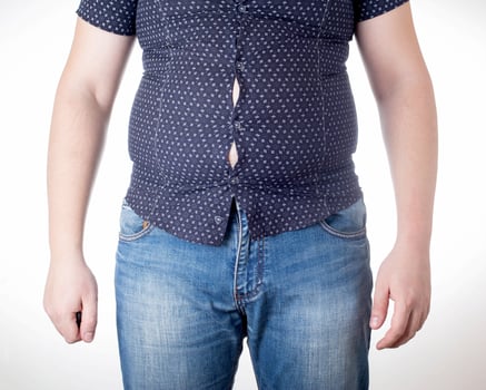 A man in a black tight shirt on a white background. Overweight, unhealthy diet and weight loss concept, close-up. Small clothing size photo