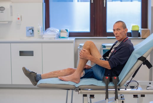 middle aged man sits anxiously on a medical couch in clinic office, waiting for the doctor to examine him and put a cast on his broken leg, professional first aid concept, photo