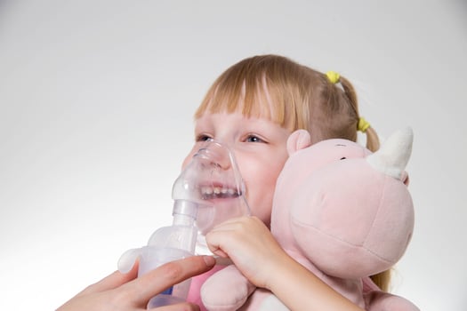 A little girl 5 years old in a pink T-shirt breathes into a nebulizer for lung disease. Treatment of bronchitis with inhalation, pharyngitis photo