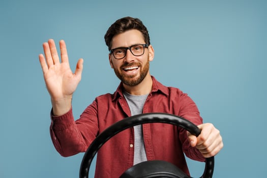 Smiling, happy bearded man, driver wearing eyeglasses holding steering wheel, waving hand photo