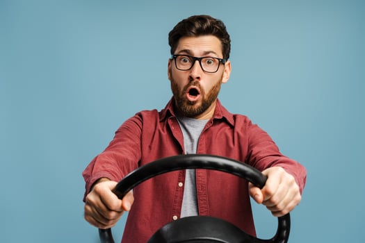Portrait of shocked, amazed bearded man wearing eyeglasses, holding steering wheel photo