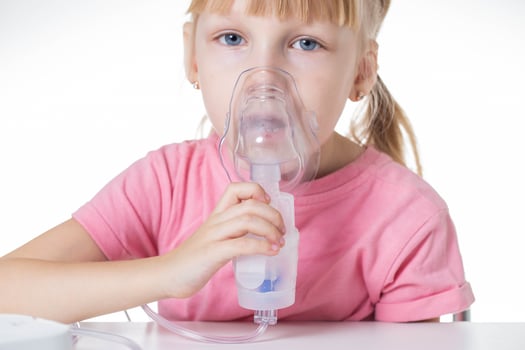 A little girl 5 years old in a pink T-shirt breathes into a nebulizer for lung disease. Treatment of bronchitis with inhalation, pharyngitis photo