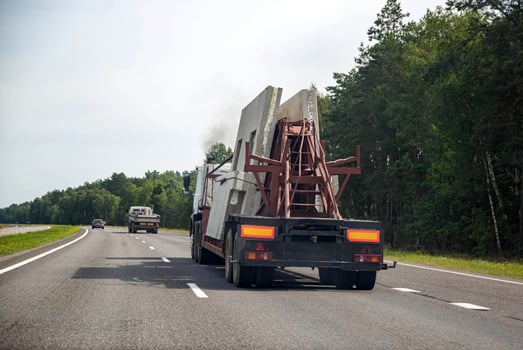 Semi-trailer truck tractor panel transporter transports reinforced concrete slabs for building a house. Transportation of spare parts for the house on the background of the forest on the highway. photo