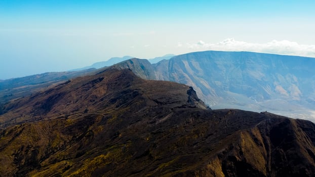 An aerial view of Mount Tambora's peak reveals a breathtaking landscape under a blue sky, as the sun rises, casting golden hues over the stunning terrain. photo