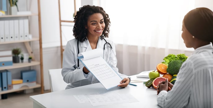 Cheerful african woman dietician showing female patient medical chart, clinic interior, empty space photo