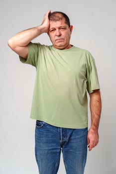A middle-aged man experiencing stress while holding his head in hands against a neutral background photo