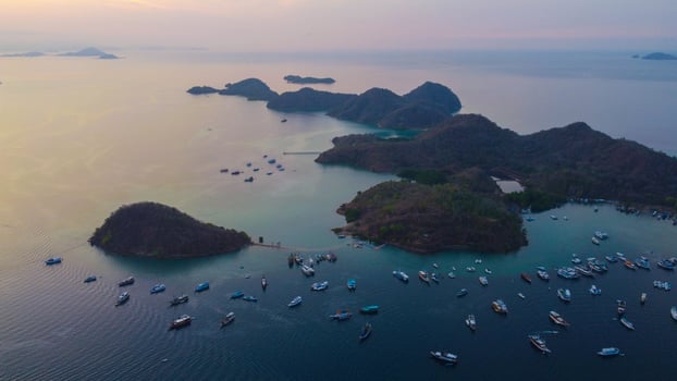 Aerial view of Labuan Bajo harbor at sunset, showcasing numerous pinisi boats docked, with charming local residences surrounding the vibrant scene. photo