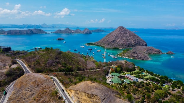 Aerial view of Labuan Bajo harbor at sunset, showcasing numerous pinisi boats docked, with charming local residences surrounding the vibrant scene. photo