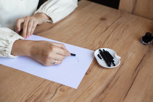 Woman Practicing Calligraphy with Black Ink and Nibs on White Paper photo