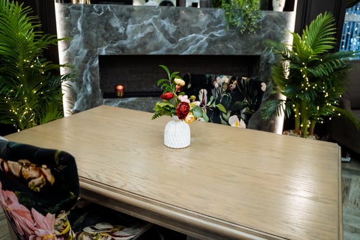 A vase of flowers sits on a table in front of a fireplace in a house photo