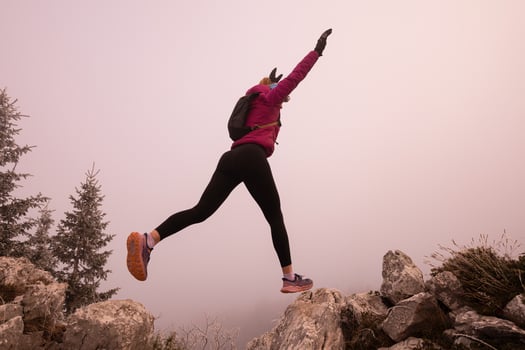 silhouette of a fitness woman trail runner jumping over a cliff and running to a rocky mountain top photo