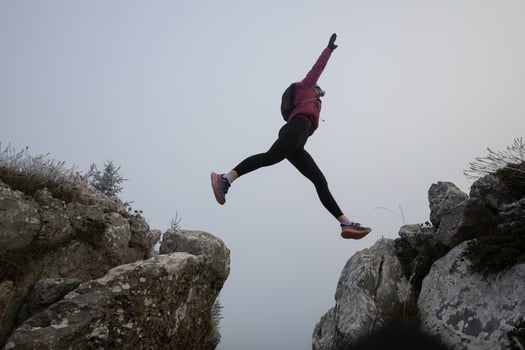 silhouette of a fitness woman trail runner jumping over a cliff and running to a rocky mountain top photo