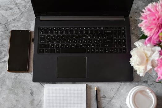 On the left side of the table lies a black smartphone, and a white disposable cup with a lidOn the right side of the table, a bouquet of pink and white peonies is visible. photo