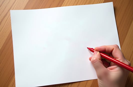 Close-up of a hand holding a red pen over a blank sheet of paper on a wooden table. Perfect for themes of creative, writing, drawing, or planning photo