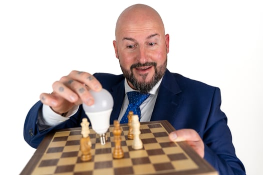 portrait of businessman in blue suit and tie with friendly expression showing light bulb on chessboard as symbol isolated on white background photo