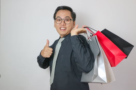 Asian office man wearing black shirt holding shopping bag giving thumbs up, isolated white office man concept photo