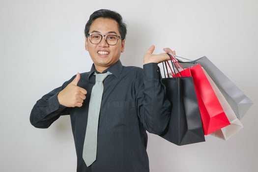 Cheerful young Asian man carrying many shopping bags on white background photo