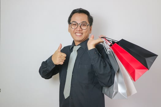 Asian man in black shirt showing thumbs up holding shopping bags, pleased with good shopping and discounts, recommending. Indoor studio shot isolated on white background photo