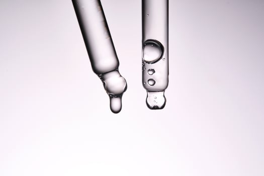 Two pipettes with a cosmetic product. Serum or fluid drips from one of them. photo