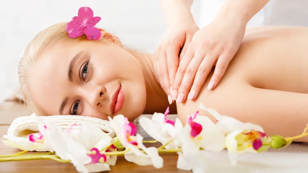 Relaxing in spa. Smiling girl lies on massage table, female hands massage shoulders, close up, free space photo
