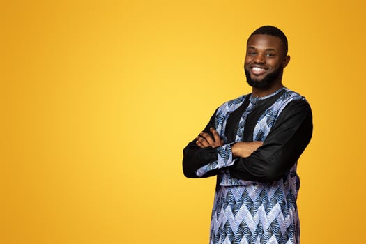 Handsome african american guy in bright traditional costume standing over pink studio background, copy space. Smiling black man posing with arms crossed, free space for text or advertisement photo