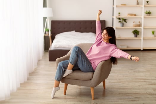 Total Relaxation And Satisfaction Concept. Portrait of beautiful relaxed woman sitting on comfortable chair, raising arms and stretching, resting on weekend day in living room. Wellness, Wellbeing photo