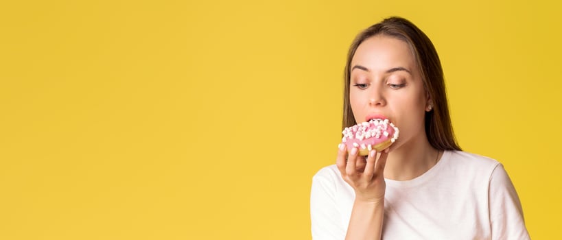 Portrait of hungry young lady eating donut isolated over yellow background with copy space photo