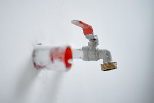 Close-up of water faucet with red handle protruding from white wall in empty apartment. Plumbing work during home renovation photo