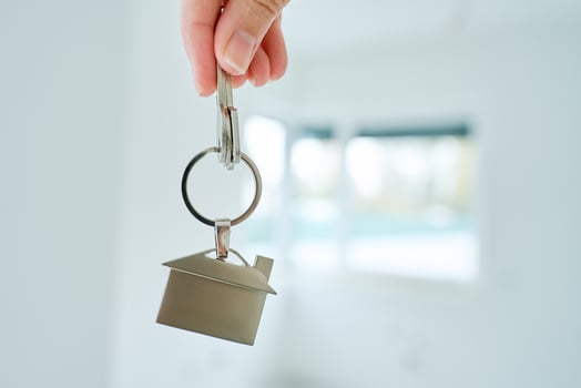 Close up hand holding keys with house shaped keychain in front of blurred new apartment interior. Concept of mortgage and new house purchase. Real estate transactions photo